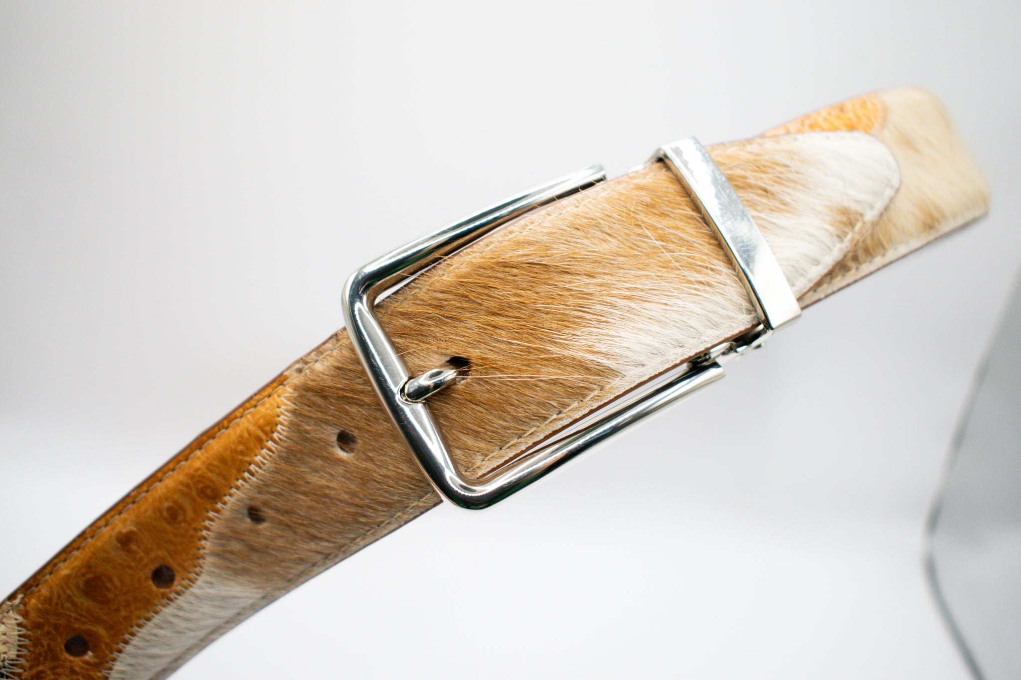Brown and white hair-on-hide belt with a silver buckle on a light gray background