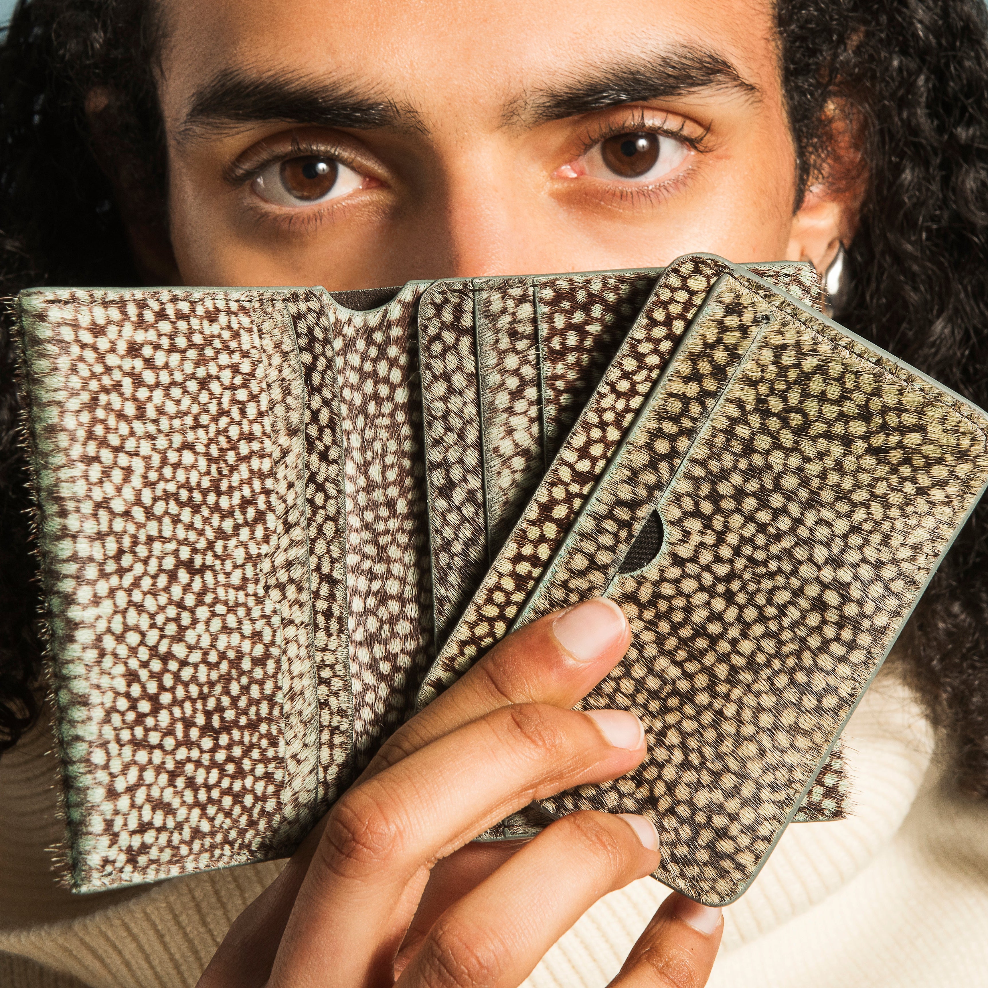 Person holding three patterned wallets in front of their face against a light blue background