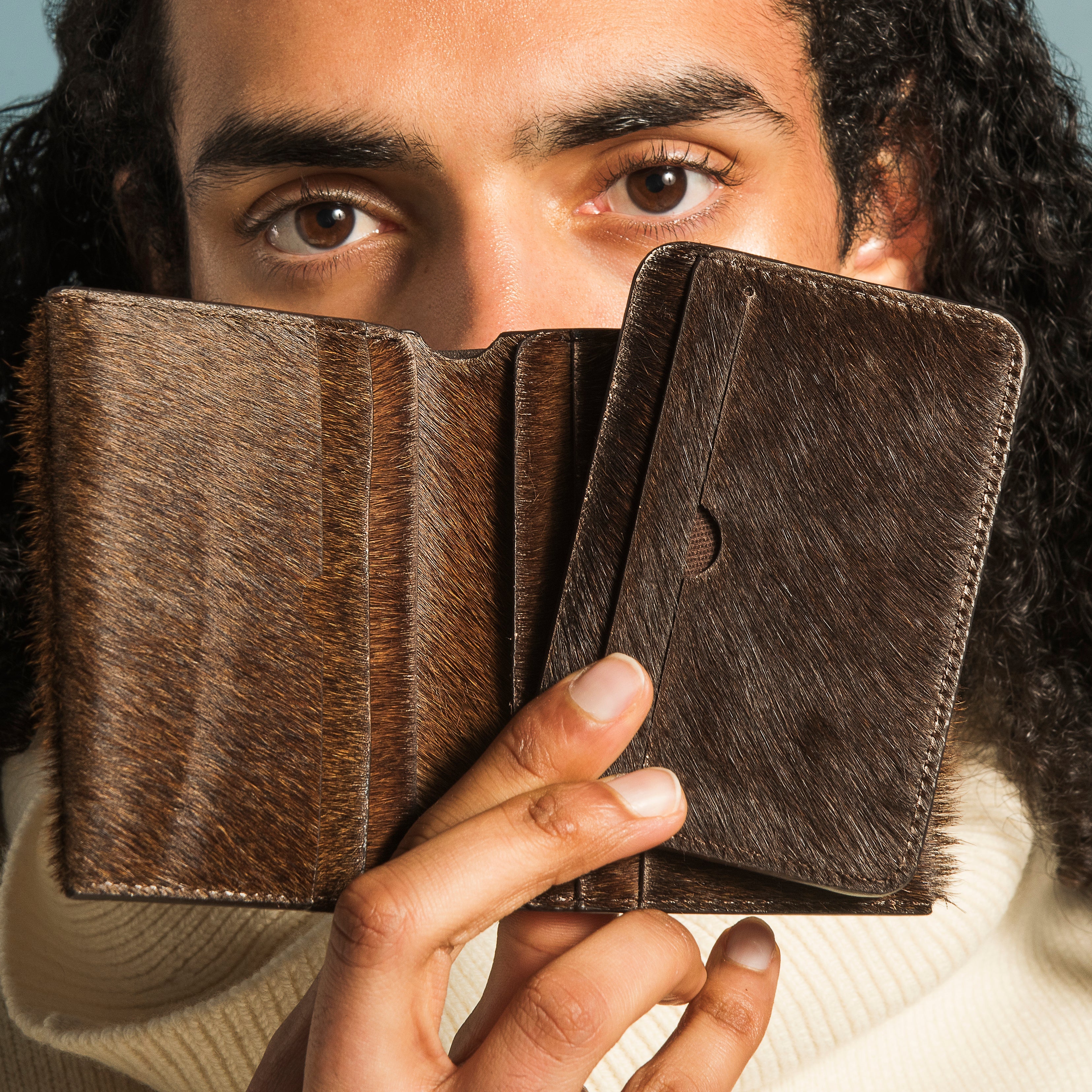 Person holding a brown leather wallet in front of their face against a light blue background